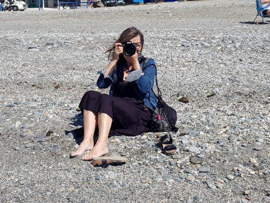 Fotografierende Frau, die am Strand sitzt