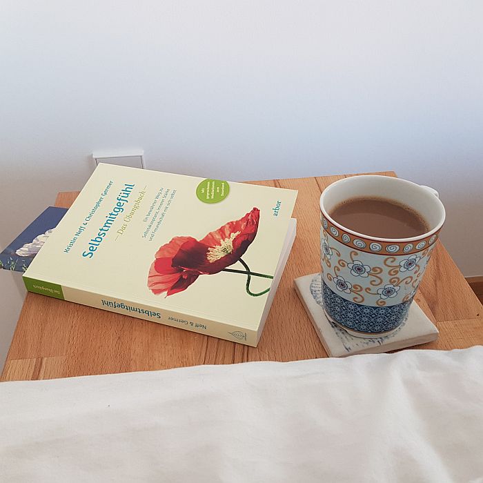 Kaffeetasse und Buch auf dem Nachttisch