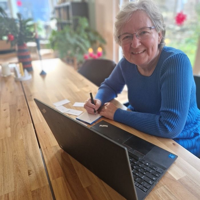 Frau im blauen Kleid mit Laptop, Stift und Zettel